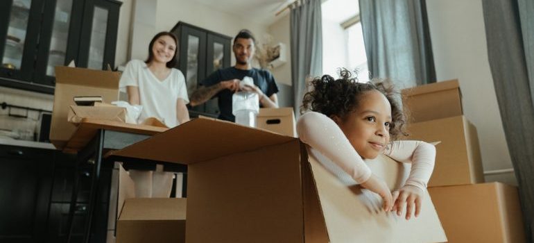 Two parents looking at their daughter sitting in a moving box while organizing a long distance move with a toddler
