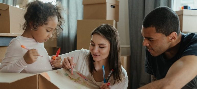 Mom, dad and a daughter draw with markers on moving boxes