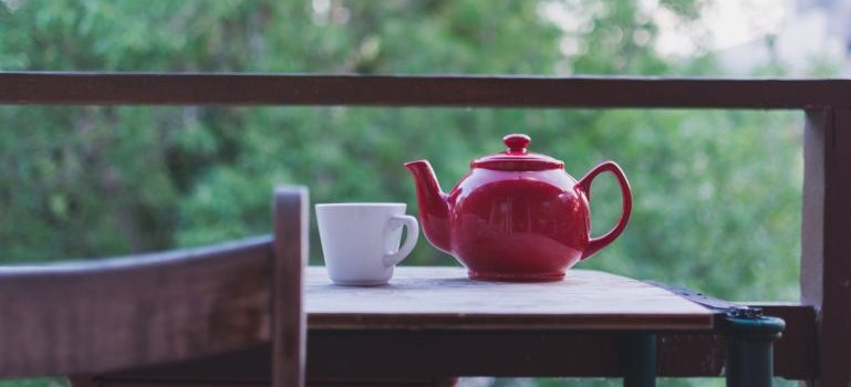 A cup and tea pot on top of a table with nature in the background