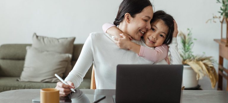 Woman working remotely while her kids hugs her