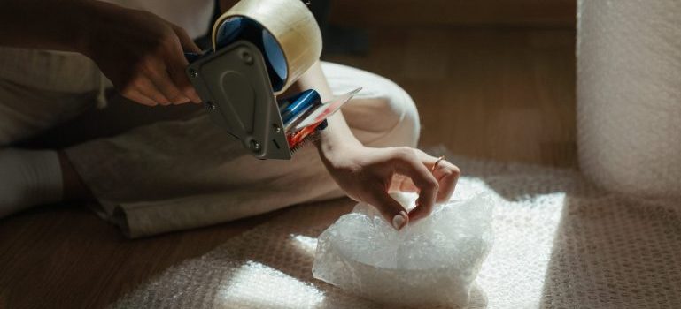 Person wrapping an item in bubble wrap and holding a tape gun