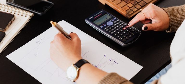 Hands using a calculator, pen and paper to calculate moving costs