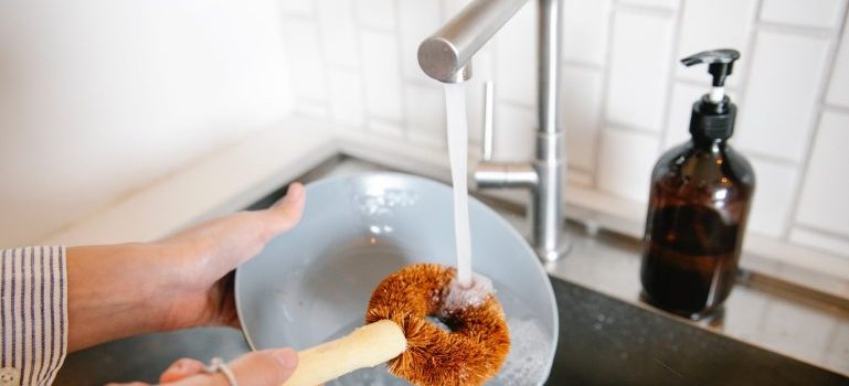 Hands washing a plate using a brush and sink water