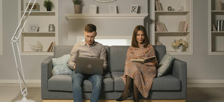 a man sitting on a couch with a woman reading a book and a laptop