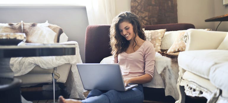 a woman sitting on the floor and reading on a laptop