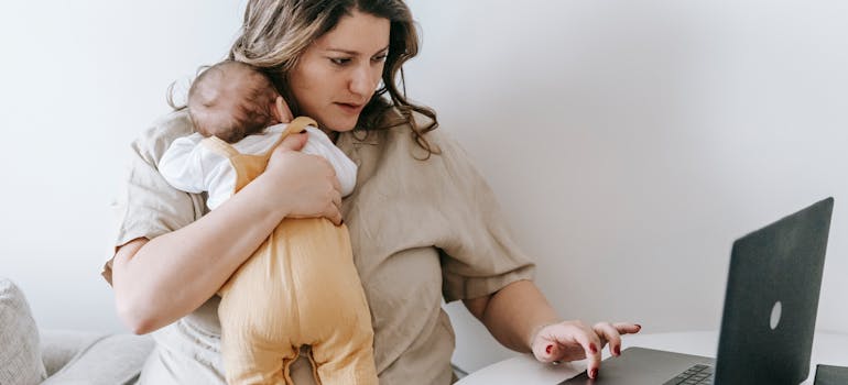 A woman holding a child while using a laptop