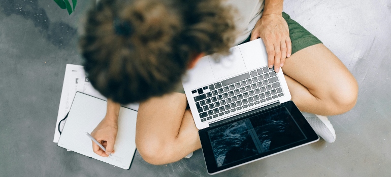 A Man Writing on a Notebook while Using a Laptop