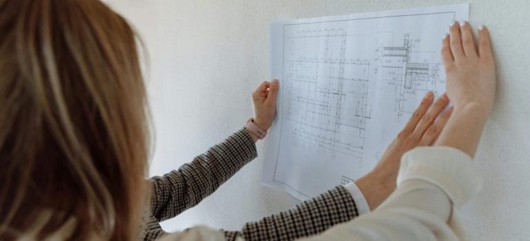 Hands holding up a home plan against the wall