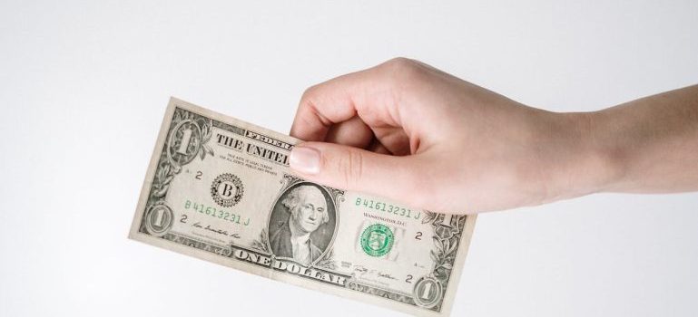 a hand holding a dollar bill to save for moving to Nepean this summer