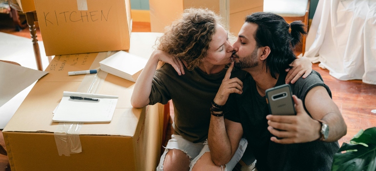 Multiracial couple kissing while taking selfie on smartphone in new home