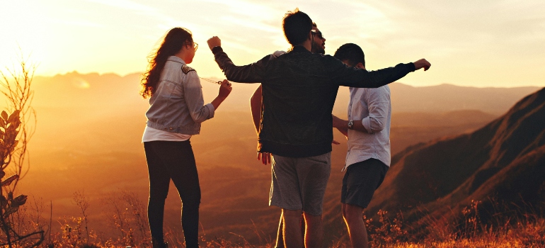 Four Person Standing at Top of Grassy Mountain