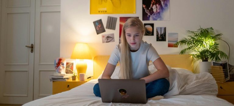 Teenage girl sitting on her bed, using laptop to explore how to prepare kids for school after moving to Ottawa