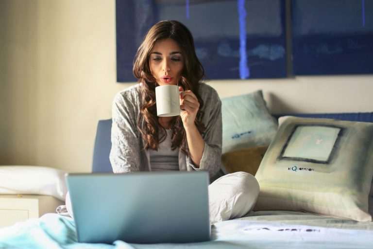 A woman drinking coffee and looking at her laptop, wondering how to find a remote job