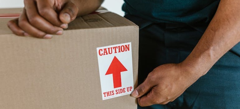 A mover standing beside a moving box with caution written on it
