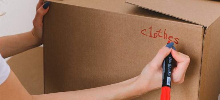 A person labeling a box where they put clothes inside