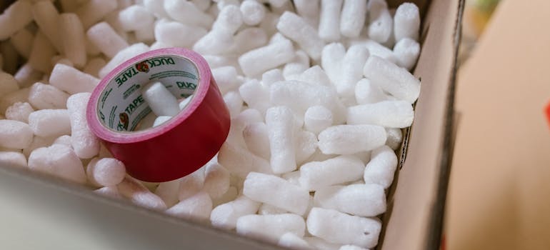 A moving box with red tape and packing peanuts inside