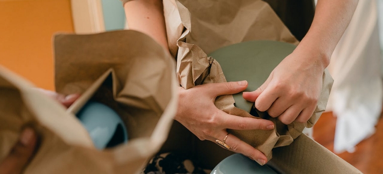 A person is packing ceramic tableware while thinking about ways to save money and time with small movers in Ottawa.
