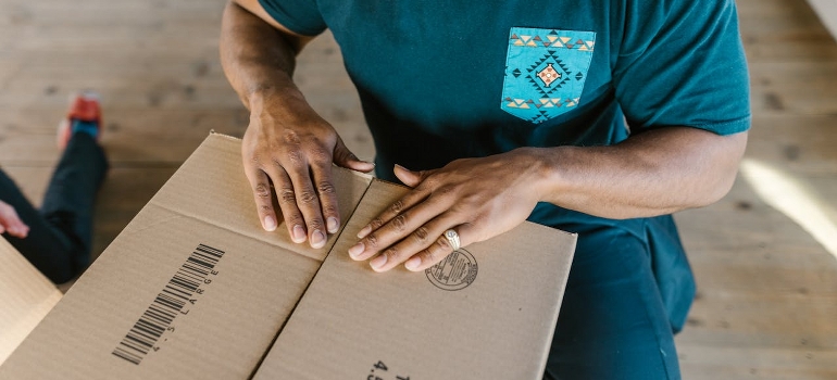 A man is closing a cardboard box with his hands. 