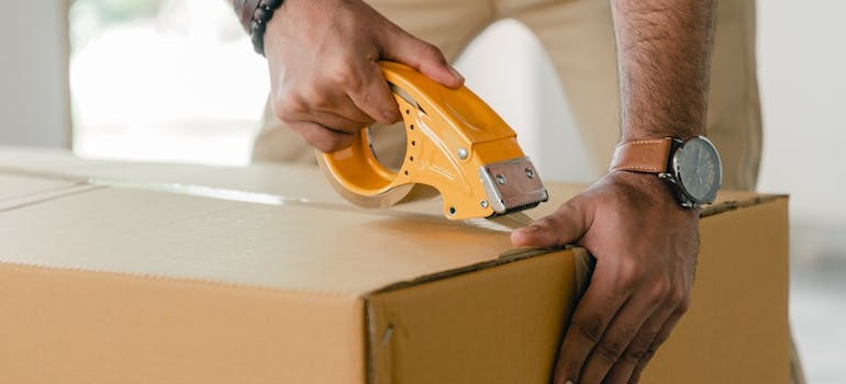 A person closing a moving box with tape