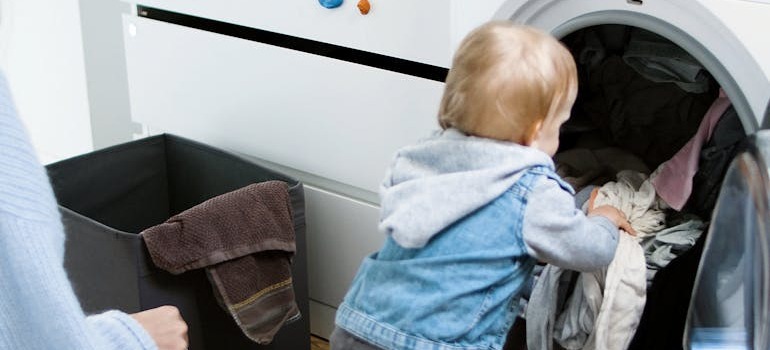 A mother with a small child putting laundry inside the washing machine
