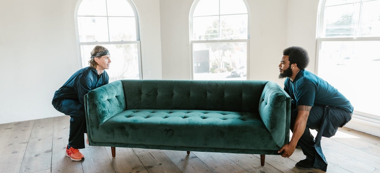 Two men are carrying a green sofa. 