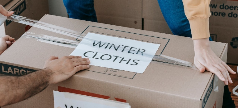 A person is closing up a labeled cardboard box. 
