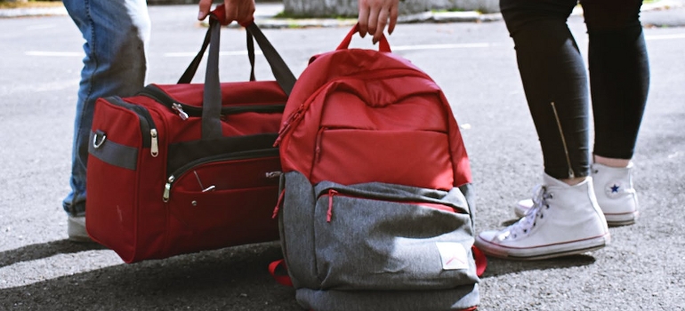 Two persons carrying a backpack and a duffel. 