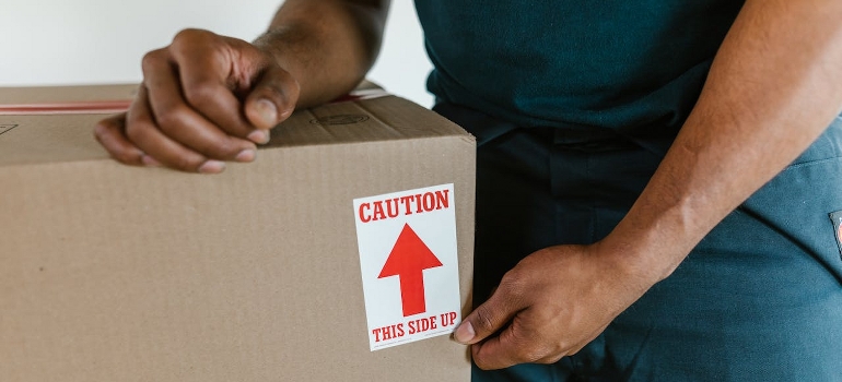 A person is holding a labeled cardboard box.