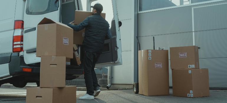 Man in Blue Jacket and Blue Denim Jeans carries a box