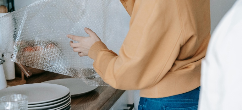 Woman in Beige Long Sleeve Shirt Wrapping Plates With Bubble Wrap
