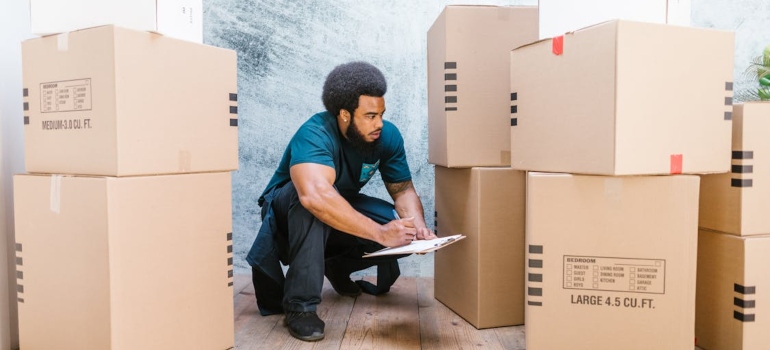 A professional mover writing on a clipboard next to boxes