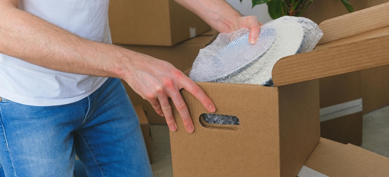 Crop of unrecognizable man packing belongings into a cardboard box before relocation, showing why Ottawa residents need storage between moves.
